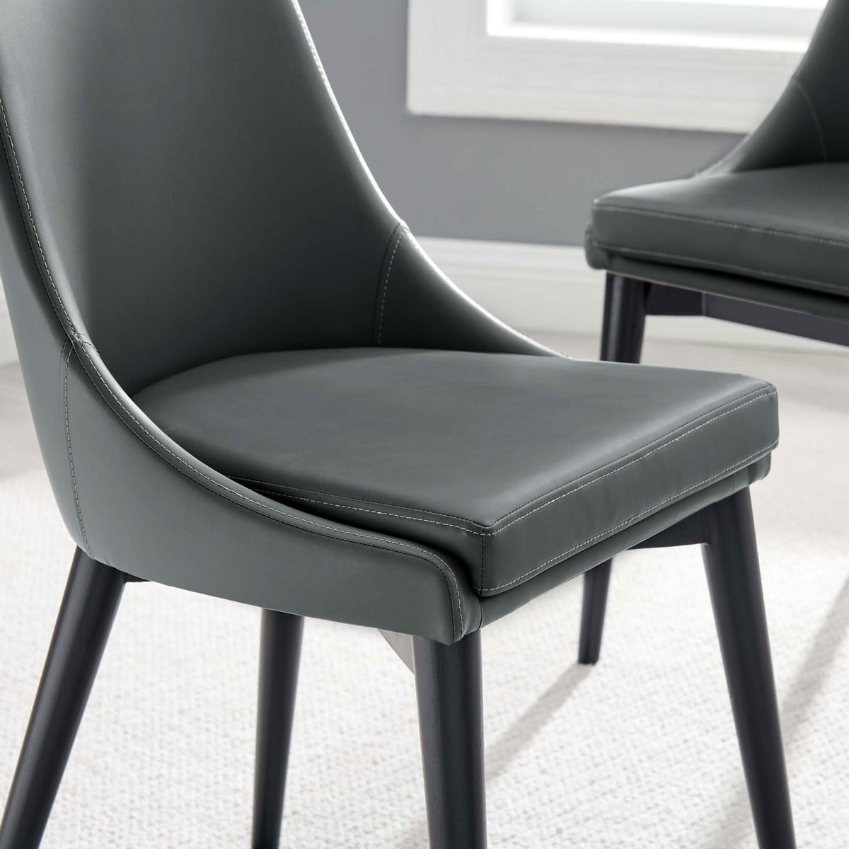 Gray vegan leather dining seat paired with a matching chair in a soft rug and window lit setting || EEI-2226-GRY || detail_room