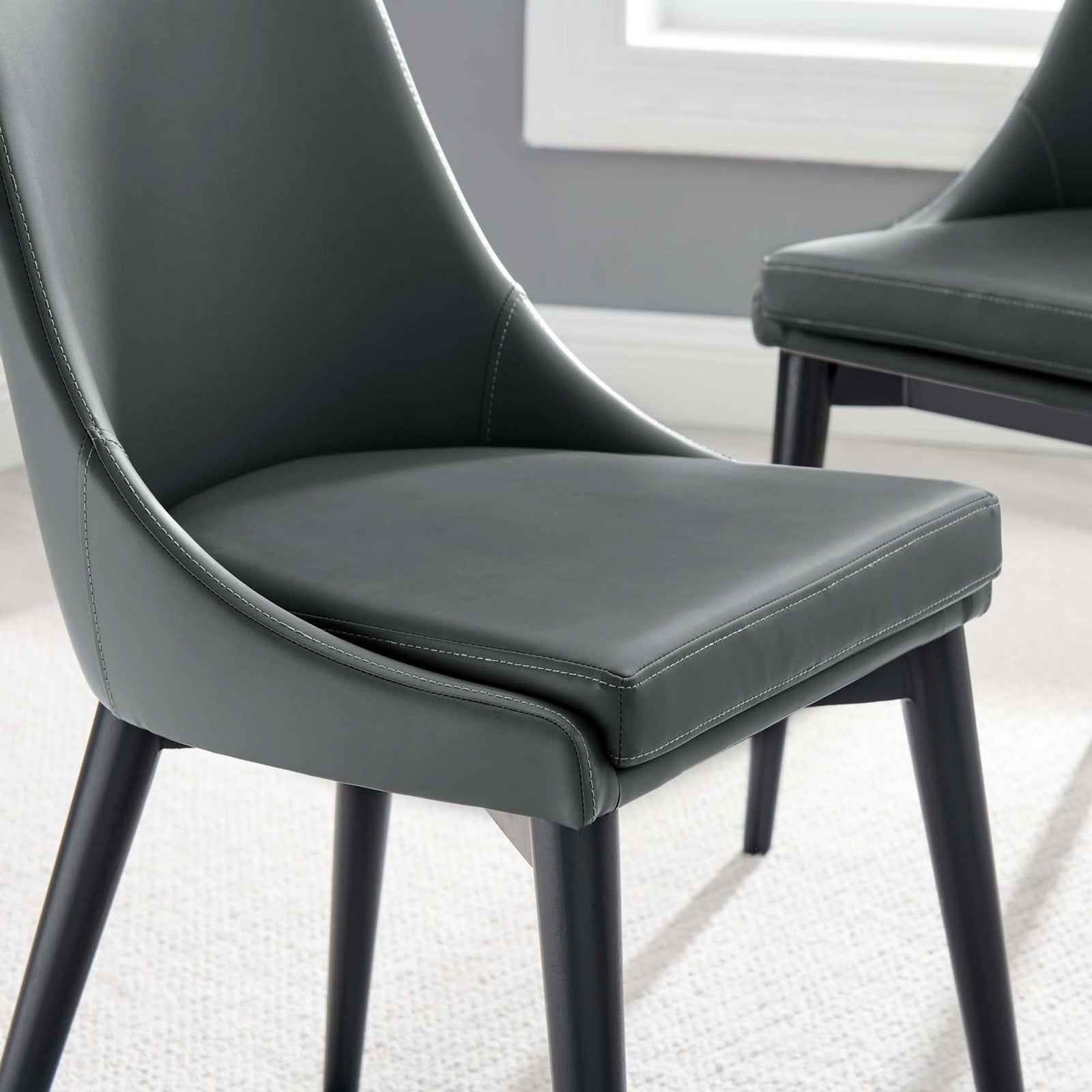 Gray vegan leather dining seat paired with a matching chair in a soft rug and window lit setting || EEI-2226-GRY || detail_room