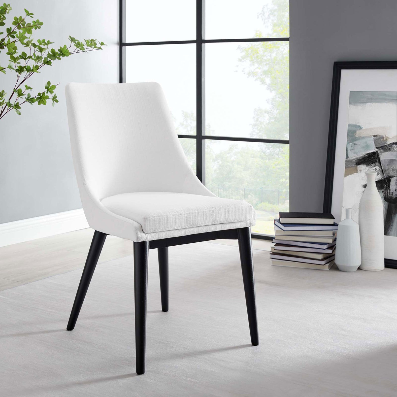 White dining chair styled beside a large window, modern artwork, and stacked books for a contemporary look || EEI-2227-WHI || front_angle_room