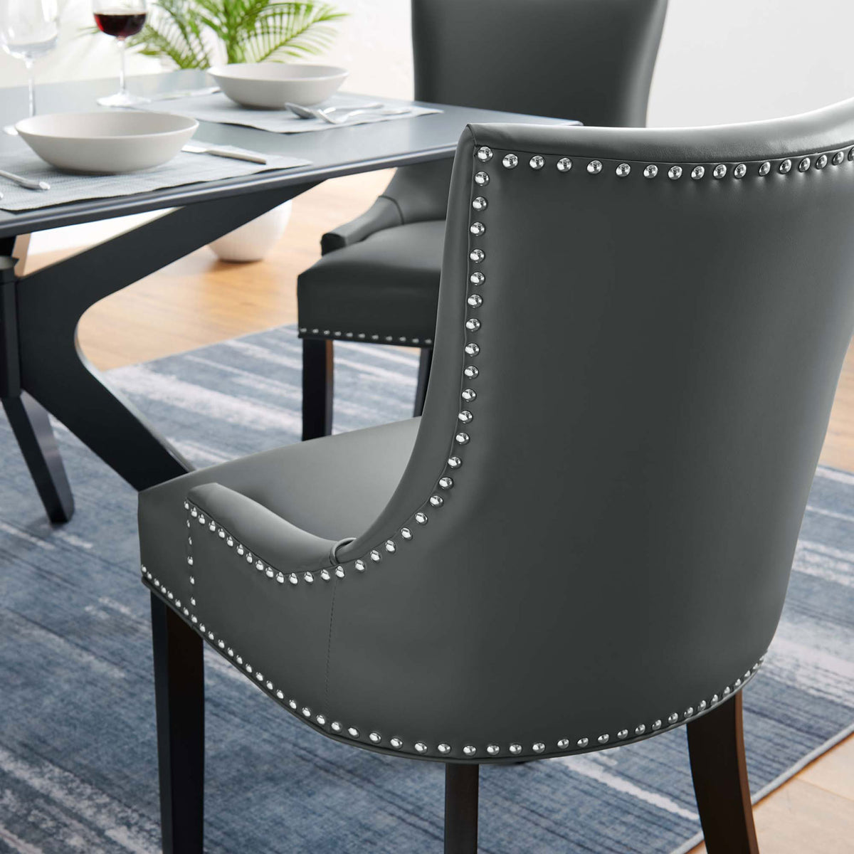 Gray vegan leather dining chair with nailhead trim styled around a dining table on a blue area rug || EEI-2228-GRY || detail_room