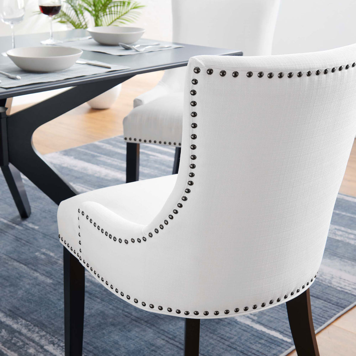 White nailhead trim dining chair paired with a modern black dining table and blue area rug || EEI-2229-WHI || detail_room