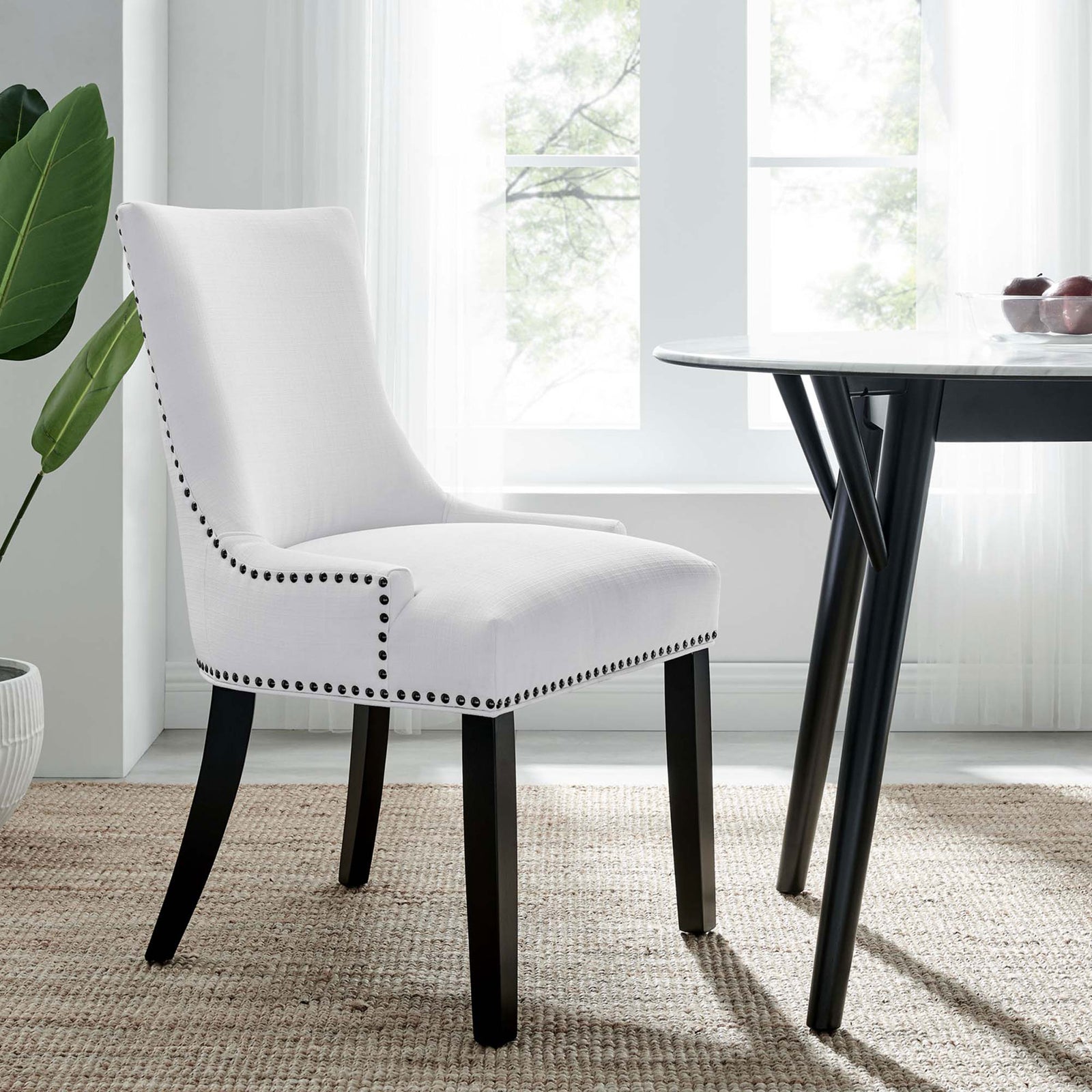 White upholstered dining chair with nailhead trim styled beside a round dining table in a bright airy room || EEI-2229-WHI || front_angle_room