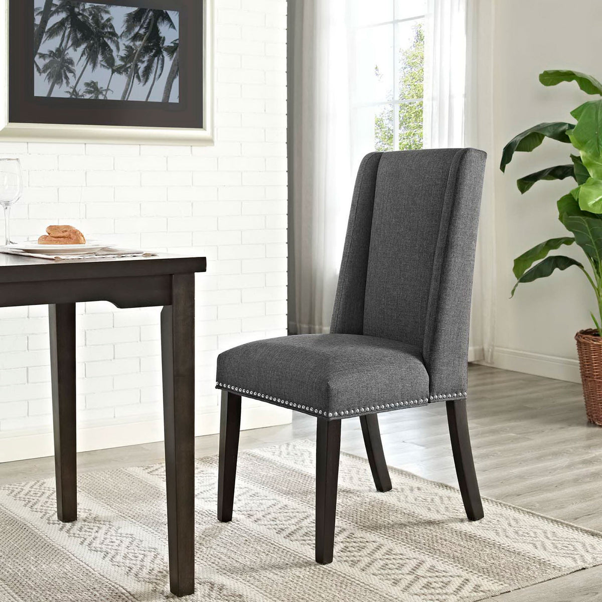 Gray upholstered dining chair styled at a dark wood table in a bright contemporary dining room. || EEI-2233-GRY || front_angle_room