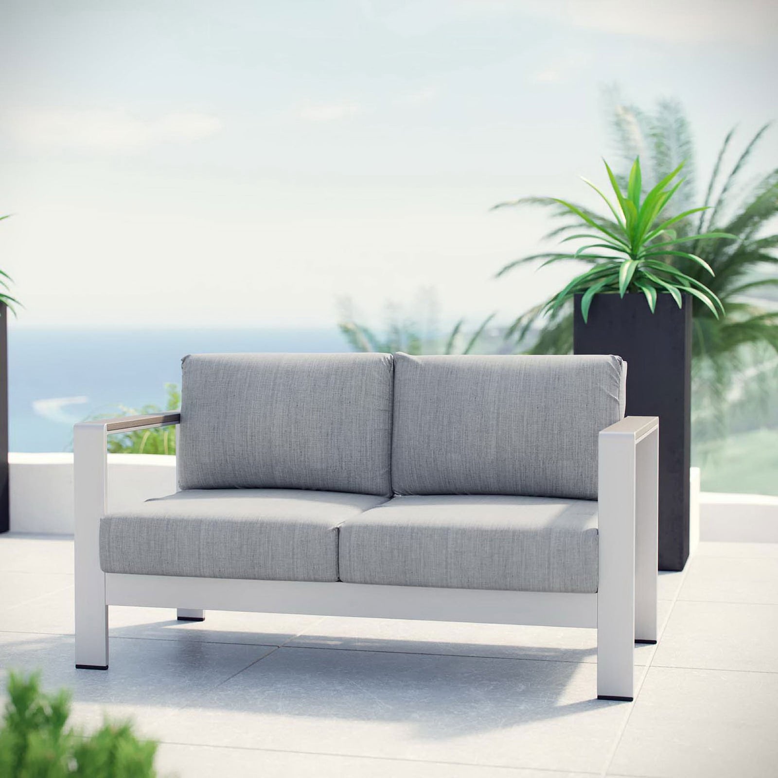 Gray cushioned aluminum loveseat styled on a sunny patio with coastal plants in the background || EEI-2267-SLV-GRY || front_room