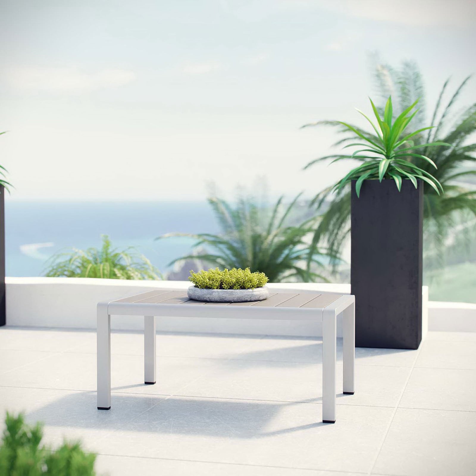 Low-profile aluminum coffee table with gray slat top styled on a sunny oceanfront terrace || EEI-2268-SLV-GRY || front_angle_room
