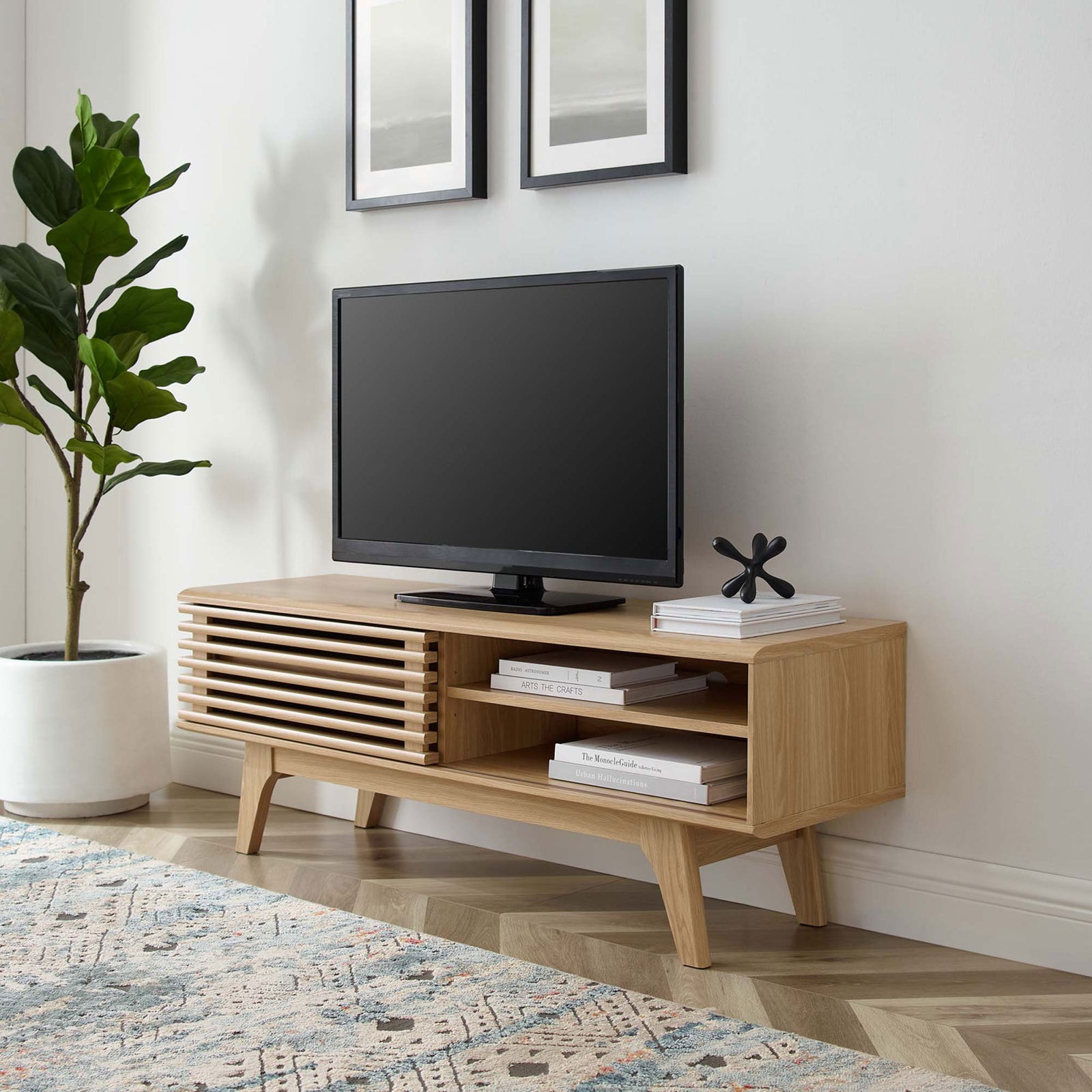 Oak mid-century TV stand anchoring a light-filled living space with artwork, rug, and leafy greenery || EEI-2539-OAK || front_angle_room
