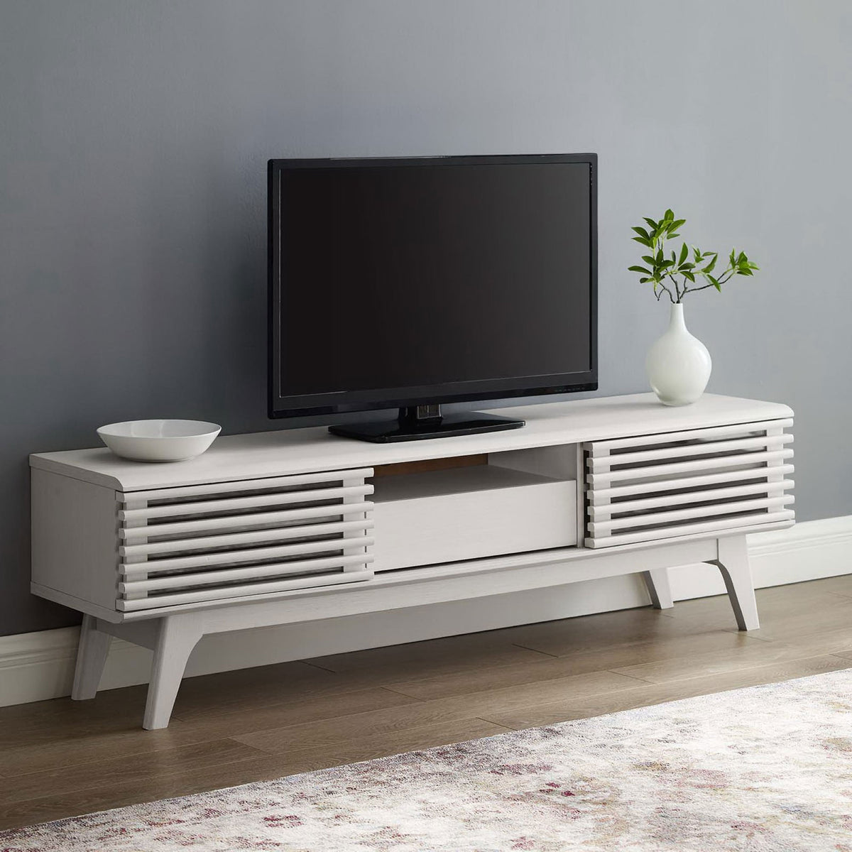 White TV stand styled in a modern living room with TV, rug, and simple decor || EEI-2541-WHI || front_angle_room