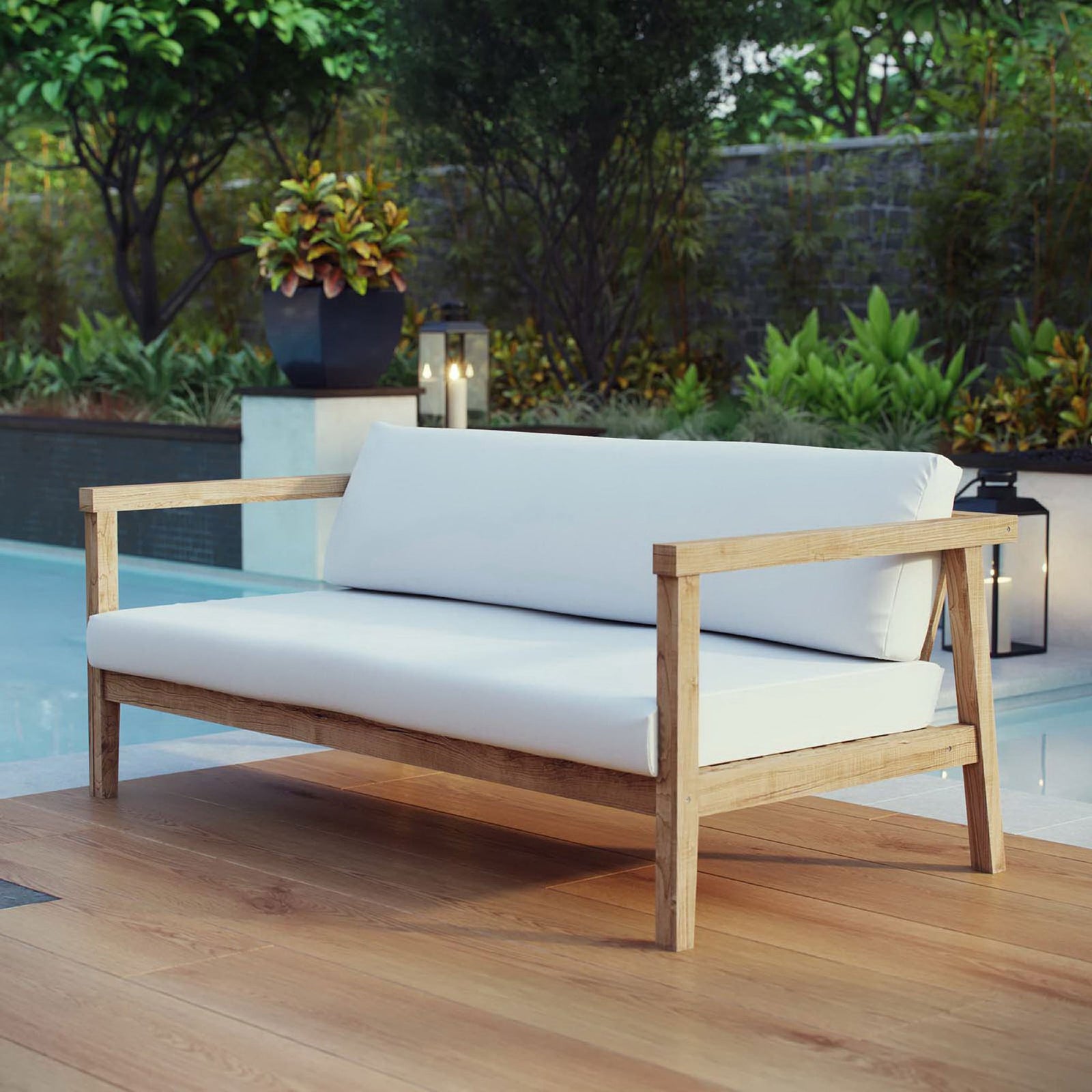 Bayport teak outdoor sofa with white cushions arranged poolside among lush greenery and lanterns || EEI-2696-NAT-WHI || front_angle_room