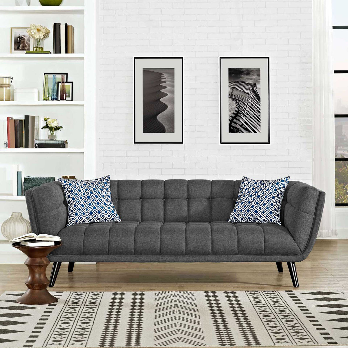 Gray tufted sofa with curved arms and slim black legs, accented by blue patterned pillows