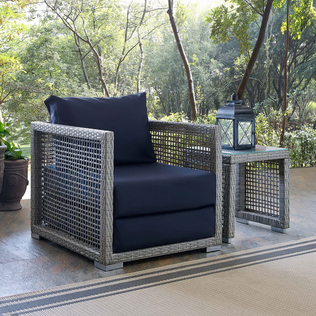 Navy cushion Aura armchair styled on a leafy patio beside a matching side table and lantern || EEI-2918-GRY-NAV || front_angle_room
