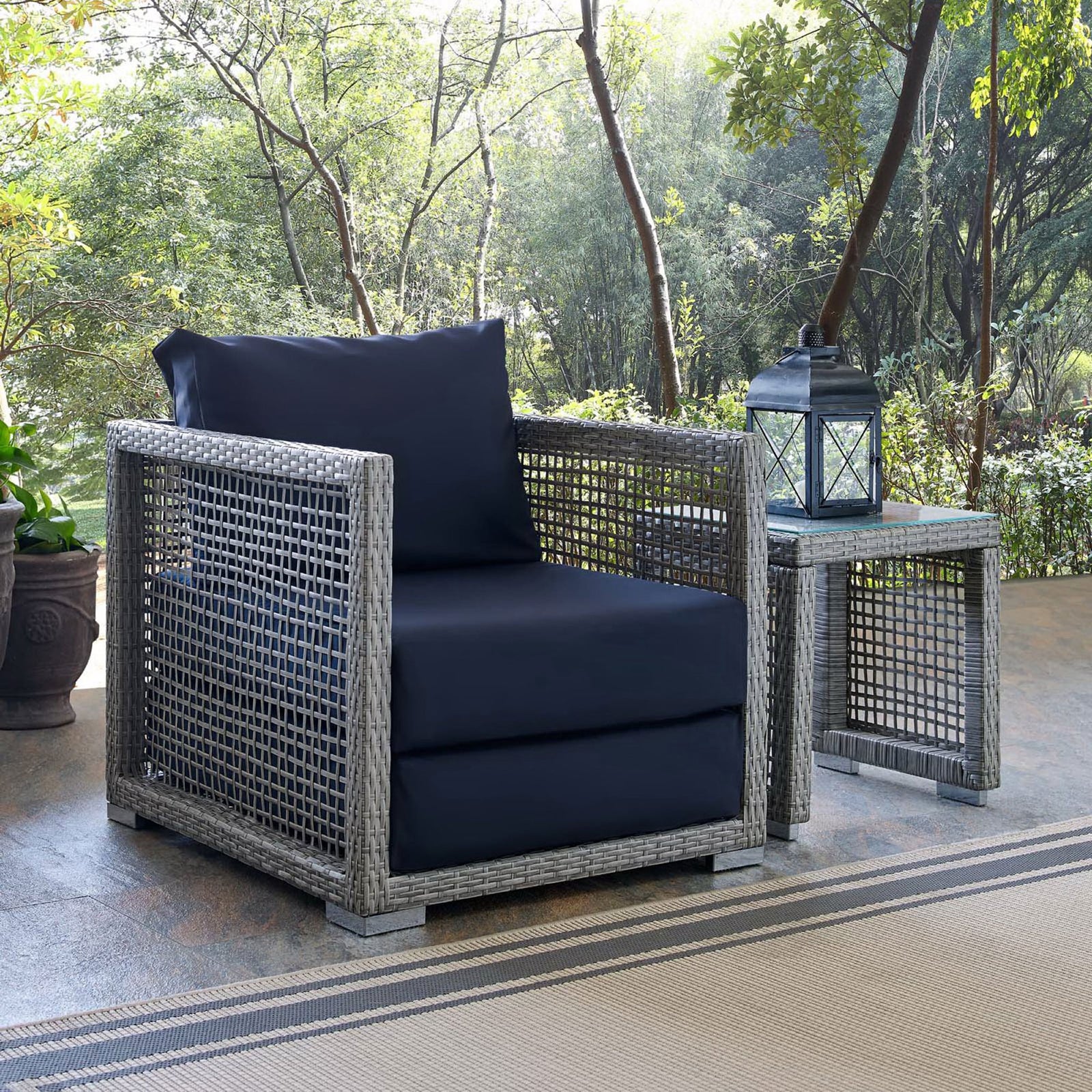 Navy cushion Aura armchair styled on a leafy patio beside a matching side table and lantern || EEI-2918-GRY-NAV || front_angle_room