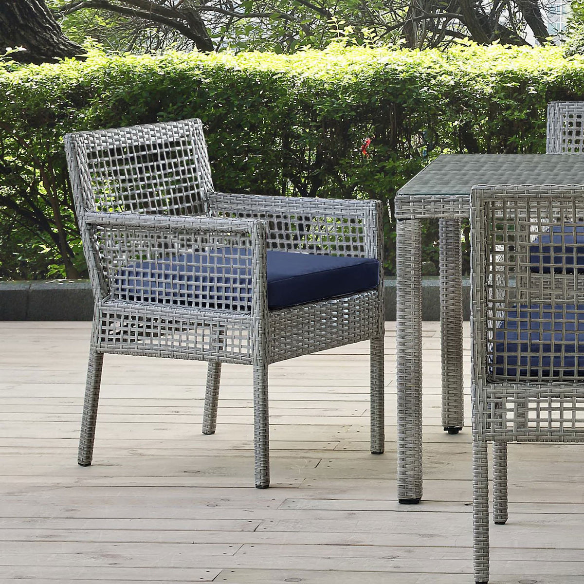 Gray wicker patio dining armchair with navy cushion arranged on an outdoor deck beside a coordinating table || EEI-2920-GRY-NAV || front_angle_room