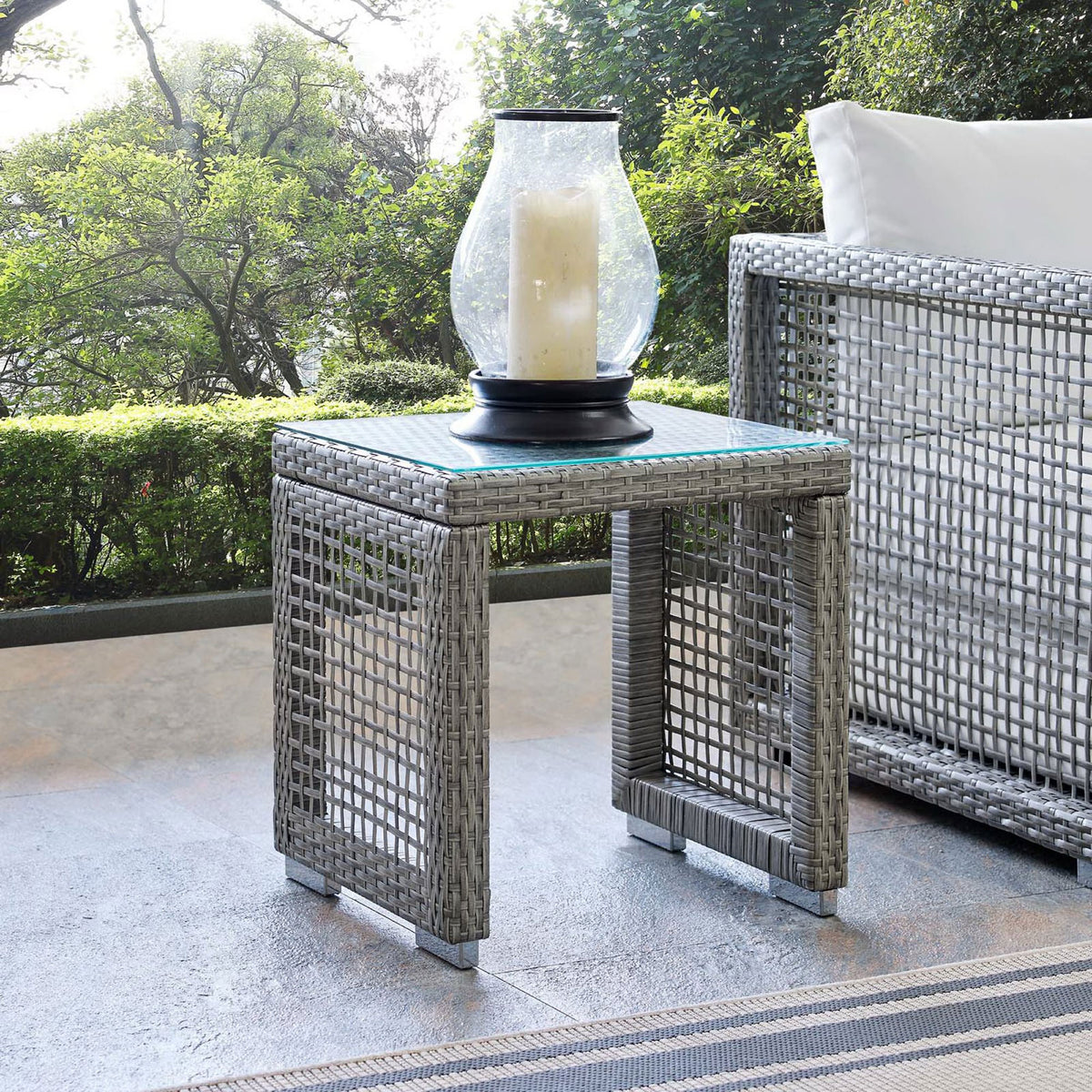 Aura gray wicker side table styled on a patio beside outdoor seating with lantern decor. || EEI-2922-GRY || front_angle_room