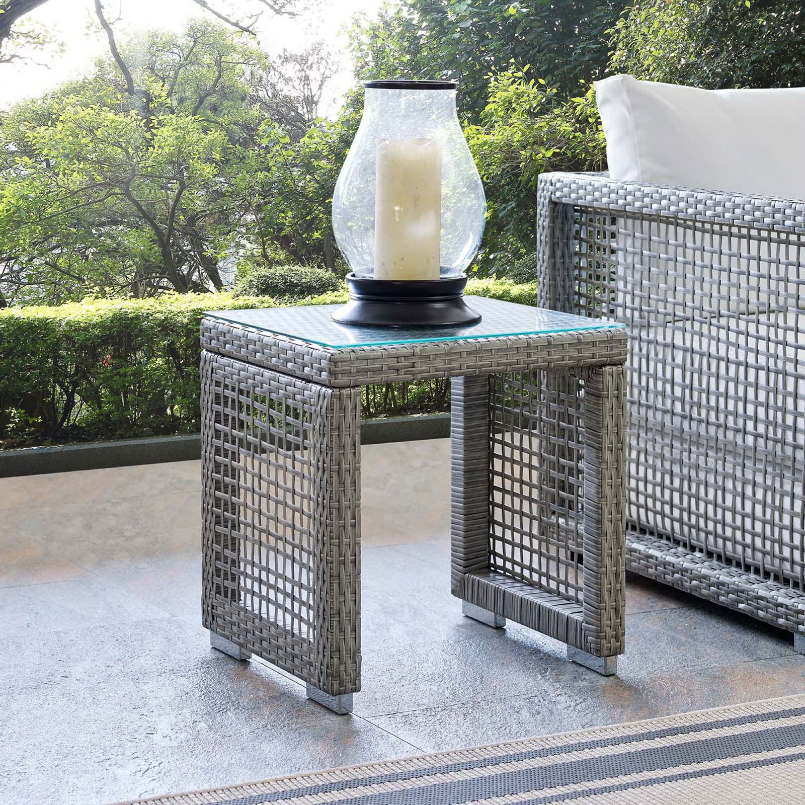 Aura gray wicker side table styled on a patio beside outdoor seating with lantern decor. || EEI-2922-GRY || front_angle_room