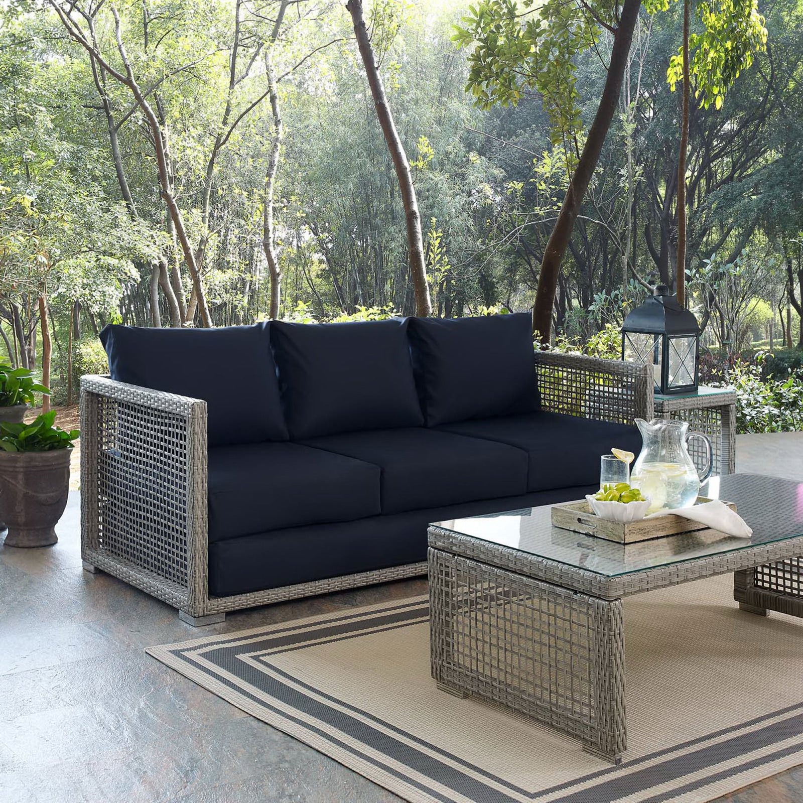 Gray wicker sofa with rich navy cushions arranged on a patio beside a matching woven coffee table || EEI-2923-GRY-NAV || front_angle_room