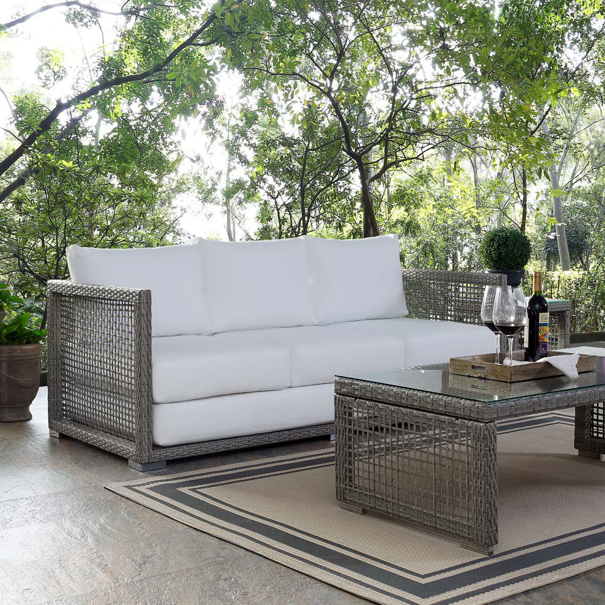 Gray wicker sofa with bright white cushions styled on a patio with coordinating woven coffee table || EEI-2923-GRY-WHI || front_angle_room