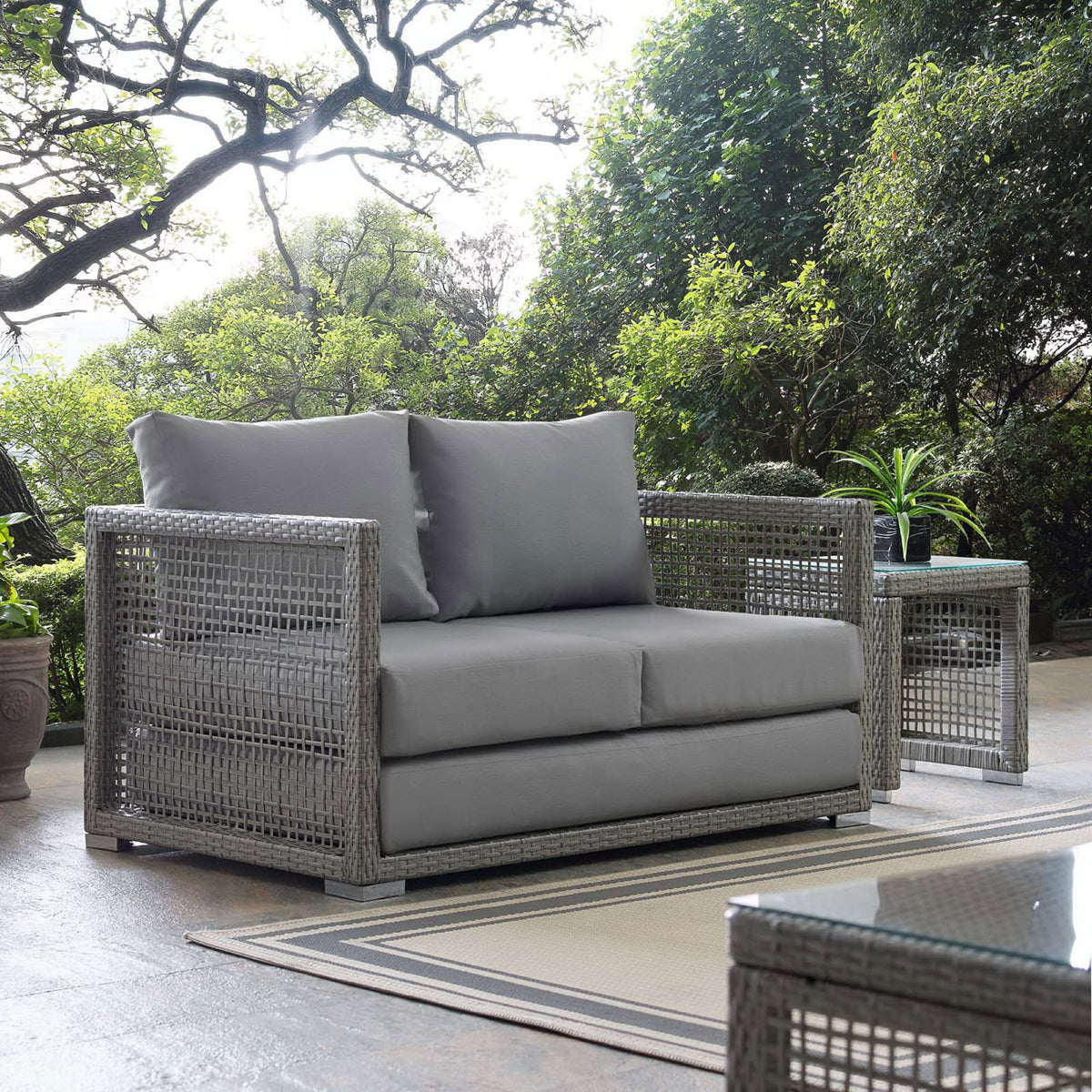 Gray wicker outdoor loveseat styled on patio with matching tables and greenery || EEI-2924-GRY-GRY || front_angle_room