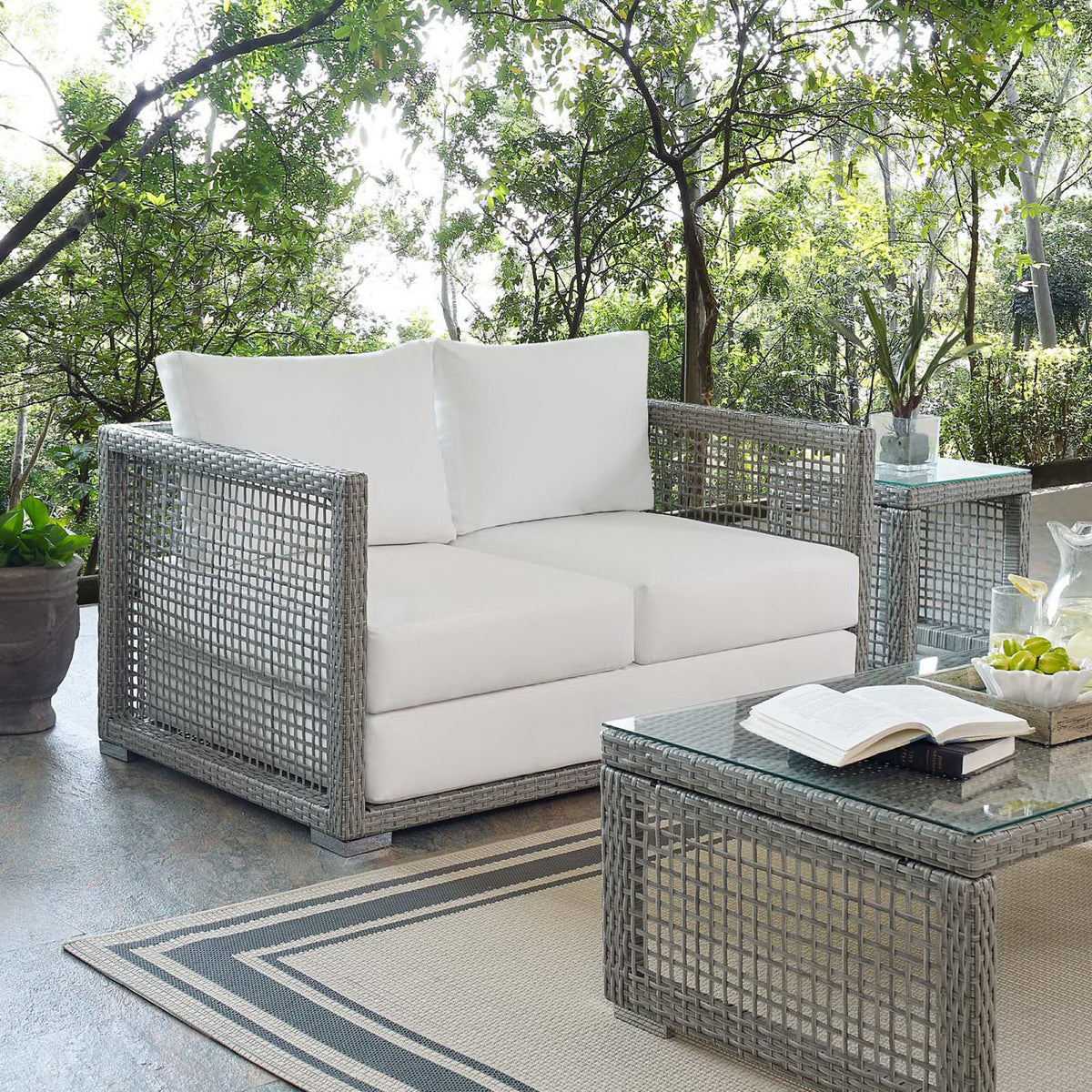 Gray wicker loveseat with white cushions styled on a bright outdoor patio || EEI-2924-GRY-WHI || front_angle_room