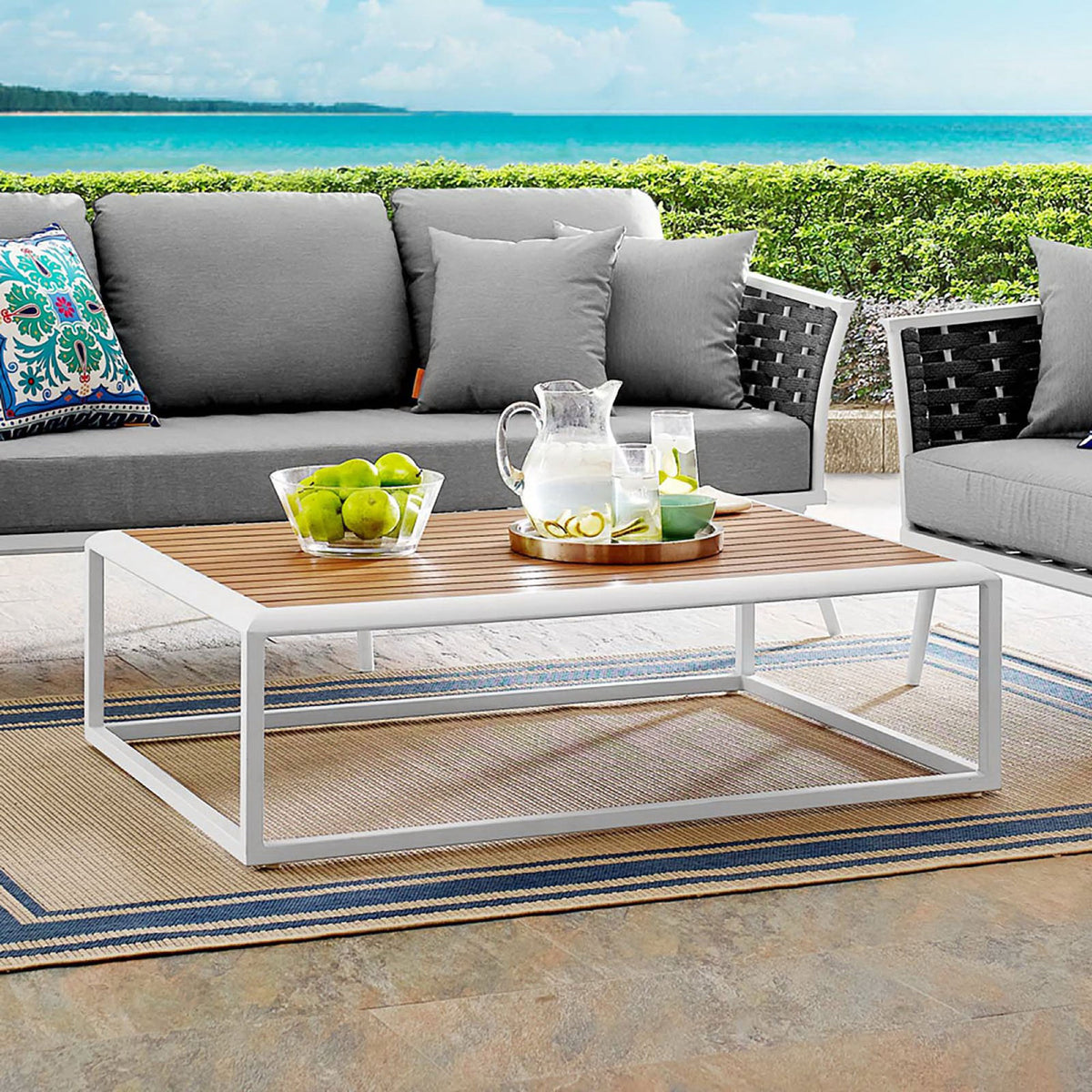 Outdoor coffee table with white frame and wood-look top styled on a coastal patio seating area. || EEI-3021-WHI-NAT || front_angle_room