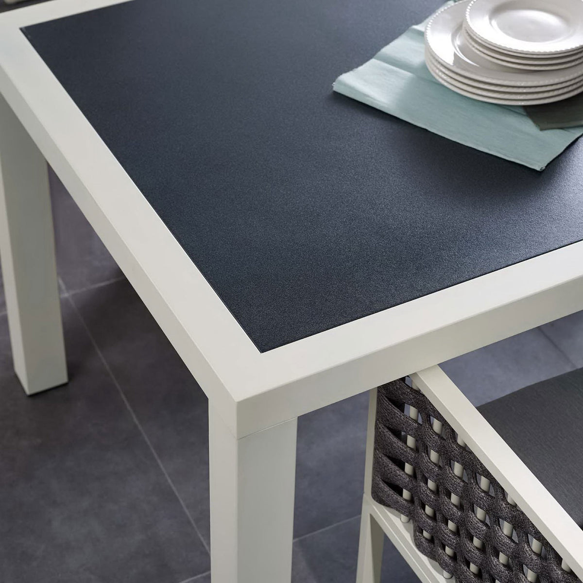 Dining table styled with outdoor dishware and woven chairs, showing the dark top against the white frame || EEI-3052-WHI-GRY || detail_room
