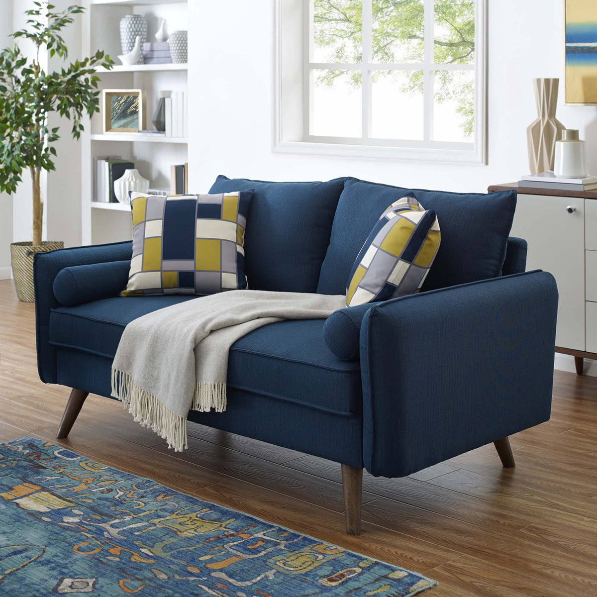 Deep blue upholstery, bolster pillows, and tapered wood legs bring comfortable style to a bright living room.