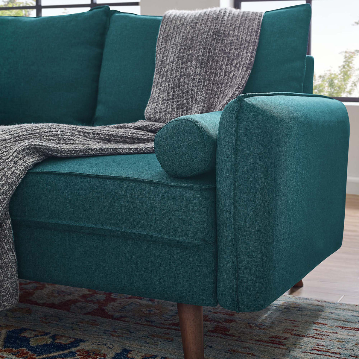 A rounded teal bolster rests against the padded arm, highlighting the loveseat's soft woven texture.