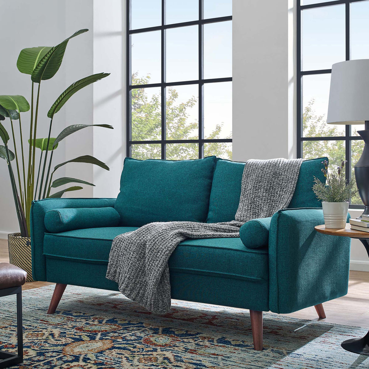 Vibrant teal fabric and tapered wood legs bring color and comfort to a light-filled living area.