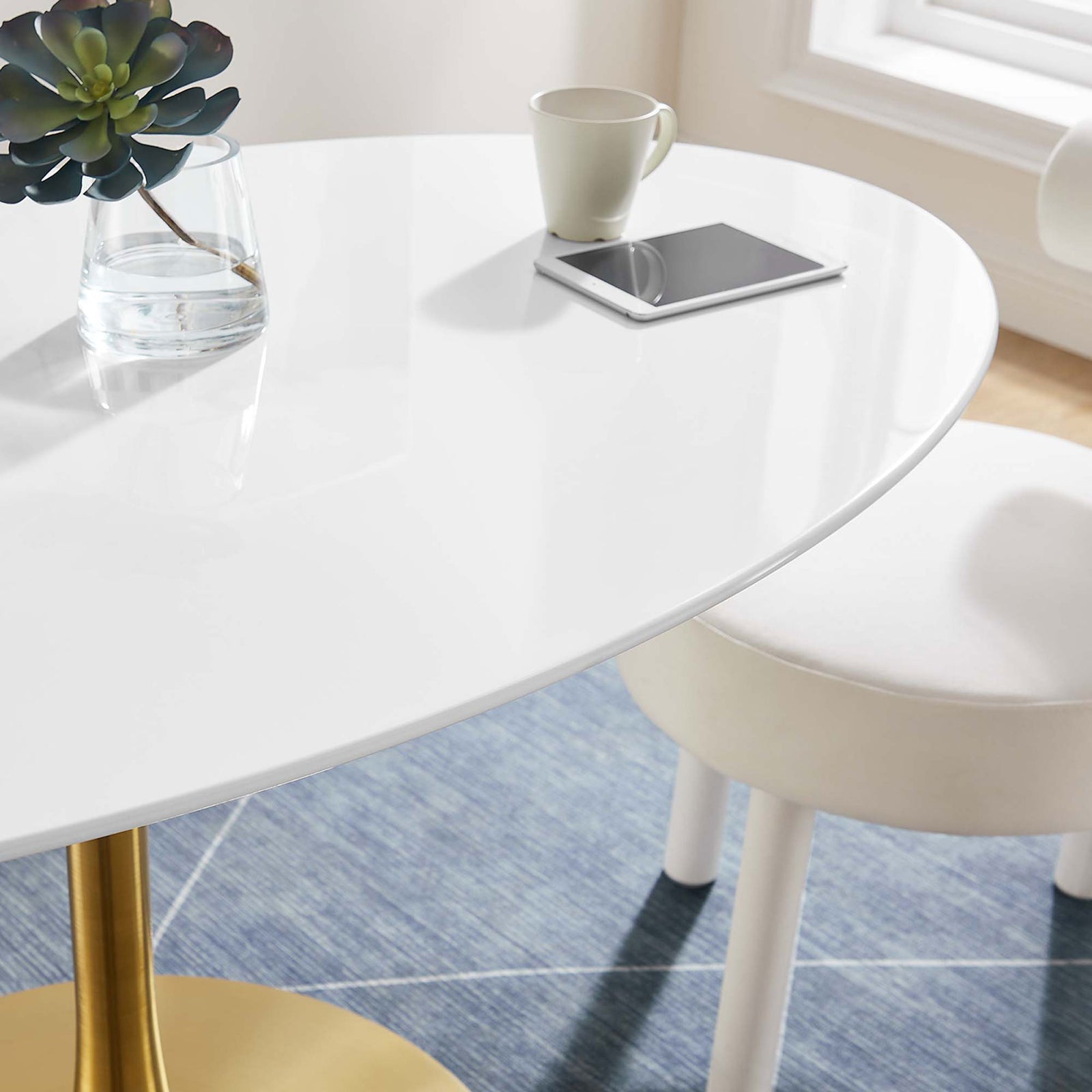 Glossy white tabletop styled with a mug, tablet, and glass vase on a textured blue area rug. || EEI-3254-GLD-WHI || detail_room