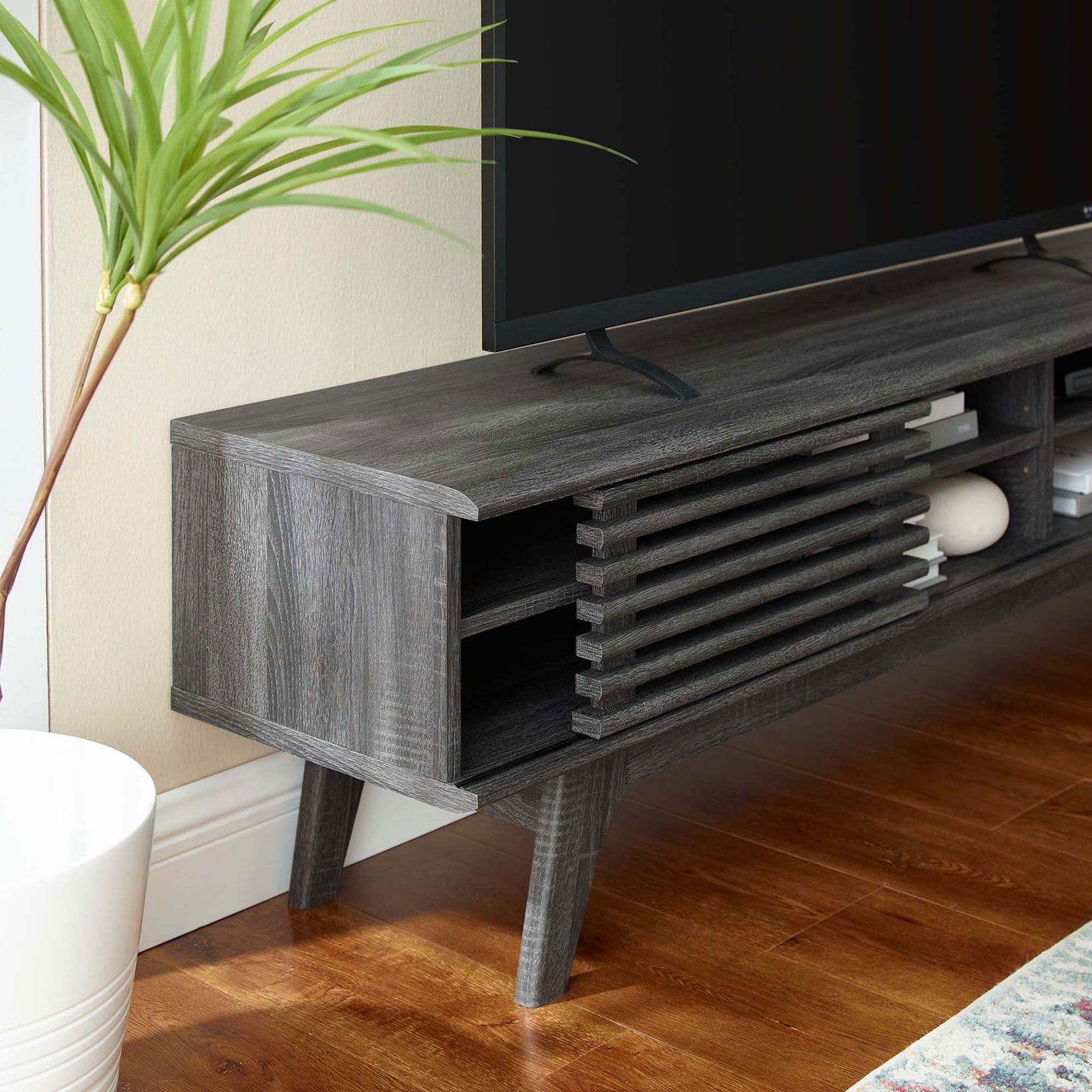 Charcoal media console end showing slatted door, open shelving, and tapered leg beside a potted plant || EEI-3303-CHA || detail_room