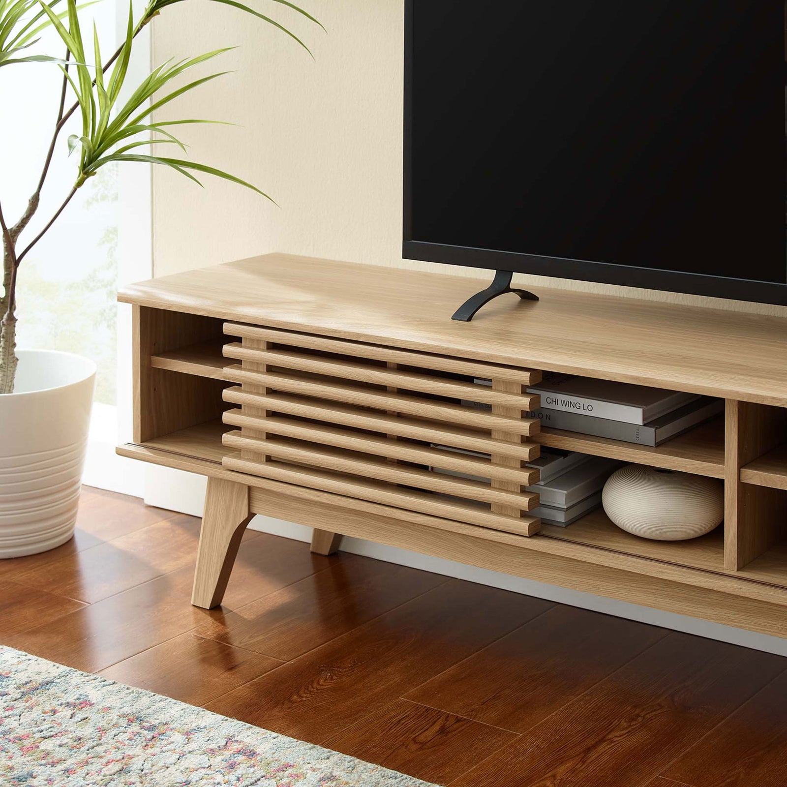 Oak media console end with slatted door, open shelf decor, and tapered leg on warm wood flooring || EEI-3303-OAK || detail_room