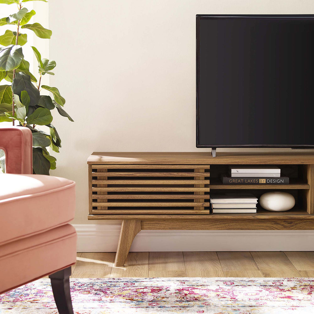 Walnut media console end with slatted door, open shelf decor, and tapered leg beside modern seating