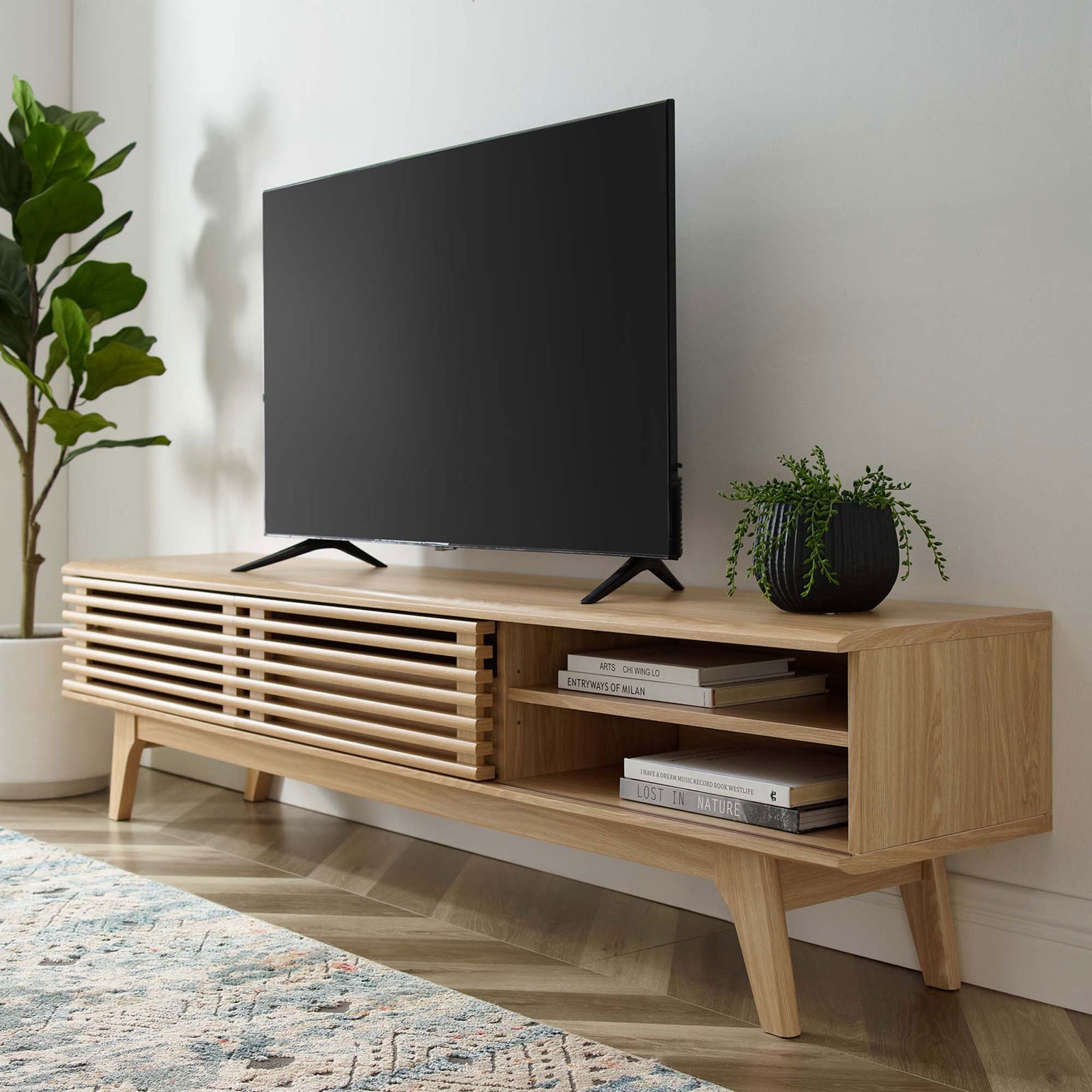 Oak TV stand in a living room with open shelf displaying stacked books and media gear || EEI-3305-OAK || front_angle_open_room