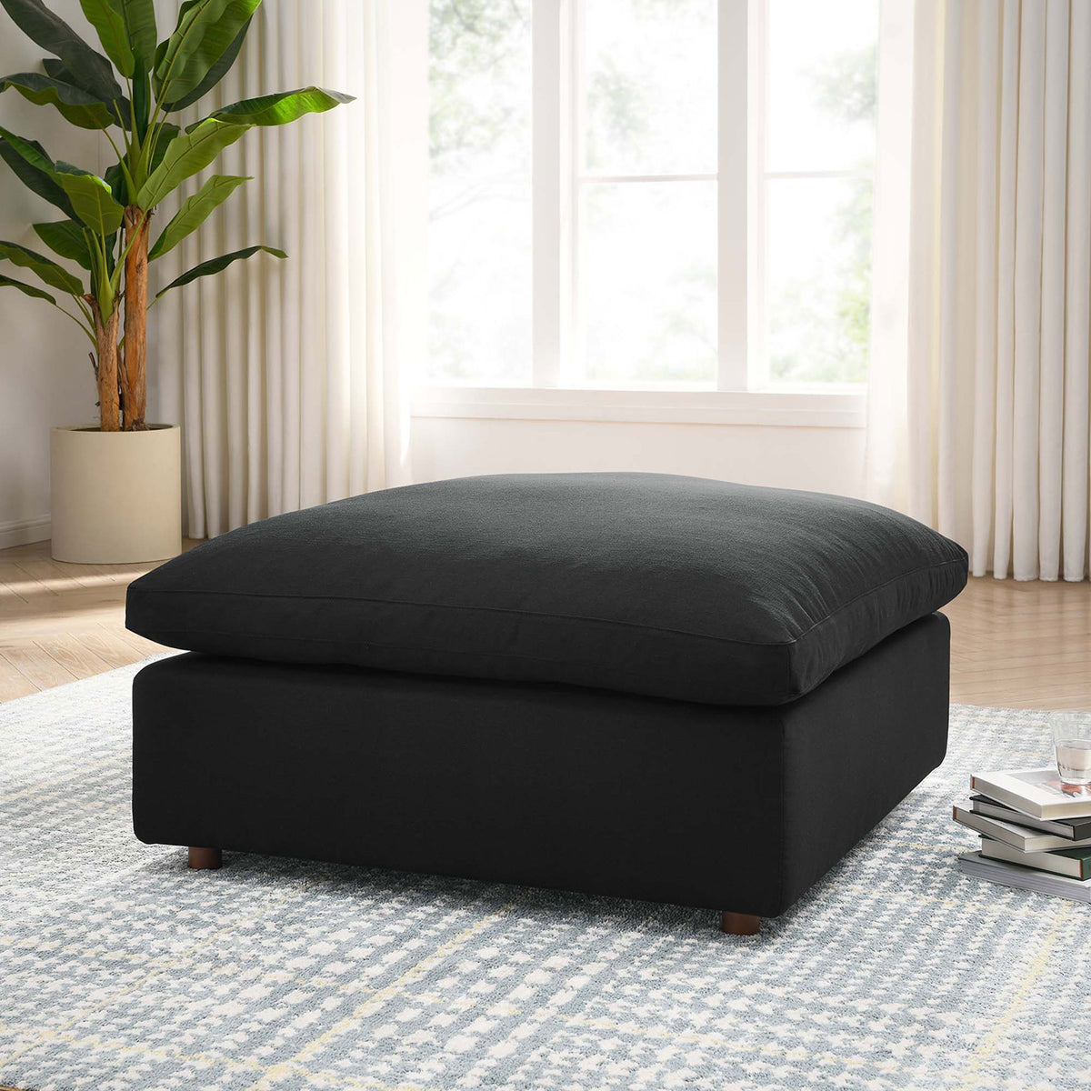 Black overstuffed ottoman styled in a bright living room, layered over a patterned rug with modern decor. || EEI-3318-BLK || front_angle_room
