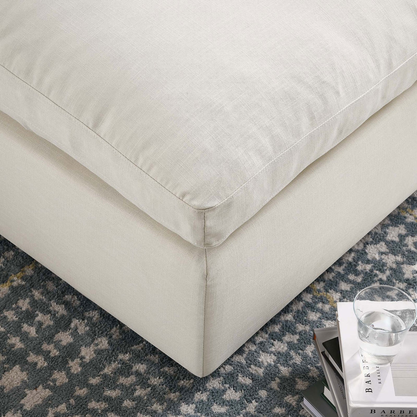 Light beige ottoman corner styled over a patterned rug, blending plush comfort with relaxed modern decor. || EEI-3318-LBG || detail_room