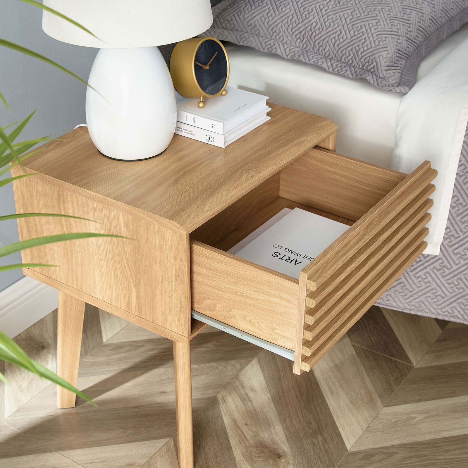Oak nightstand beside a bed with open drawer and neatly arranged books and decor || EEI-3345-OAK || front_angle_open_room