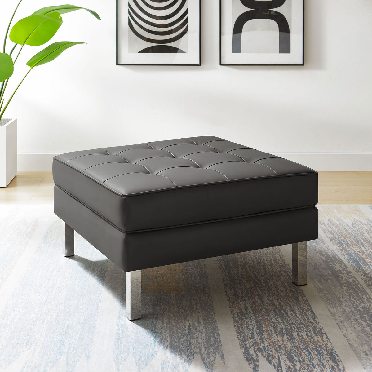 Silver gray tufted vegan leather ottoman on chrome legs styled in a modern living room with art and area rug || EEI-3394-SLV-GRY || front_angle_room