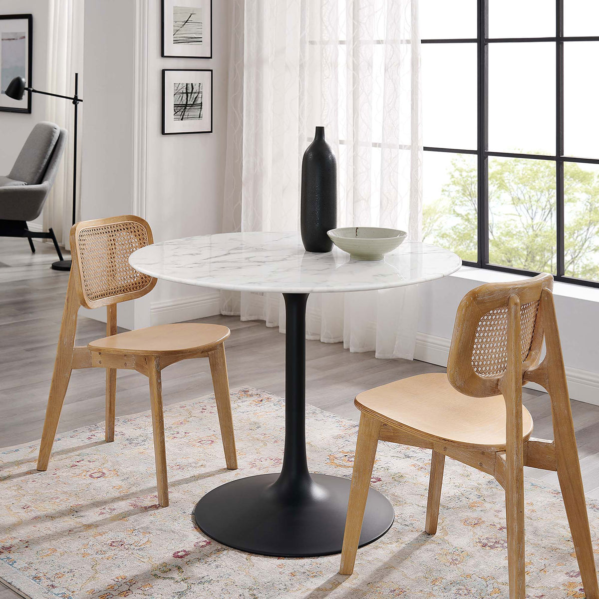 Round faux marble dining table paired with two woven back chairs in a light filled modern room || EEI-3526-BLK-WHI || front_angle_room
