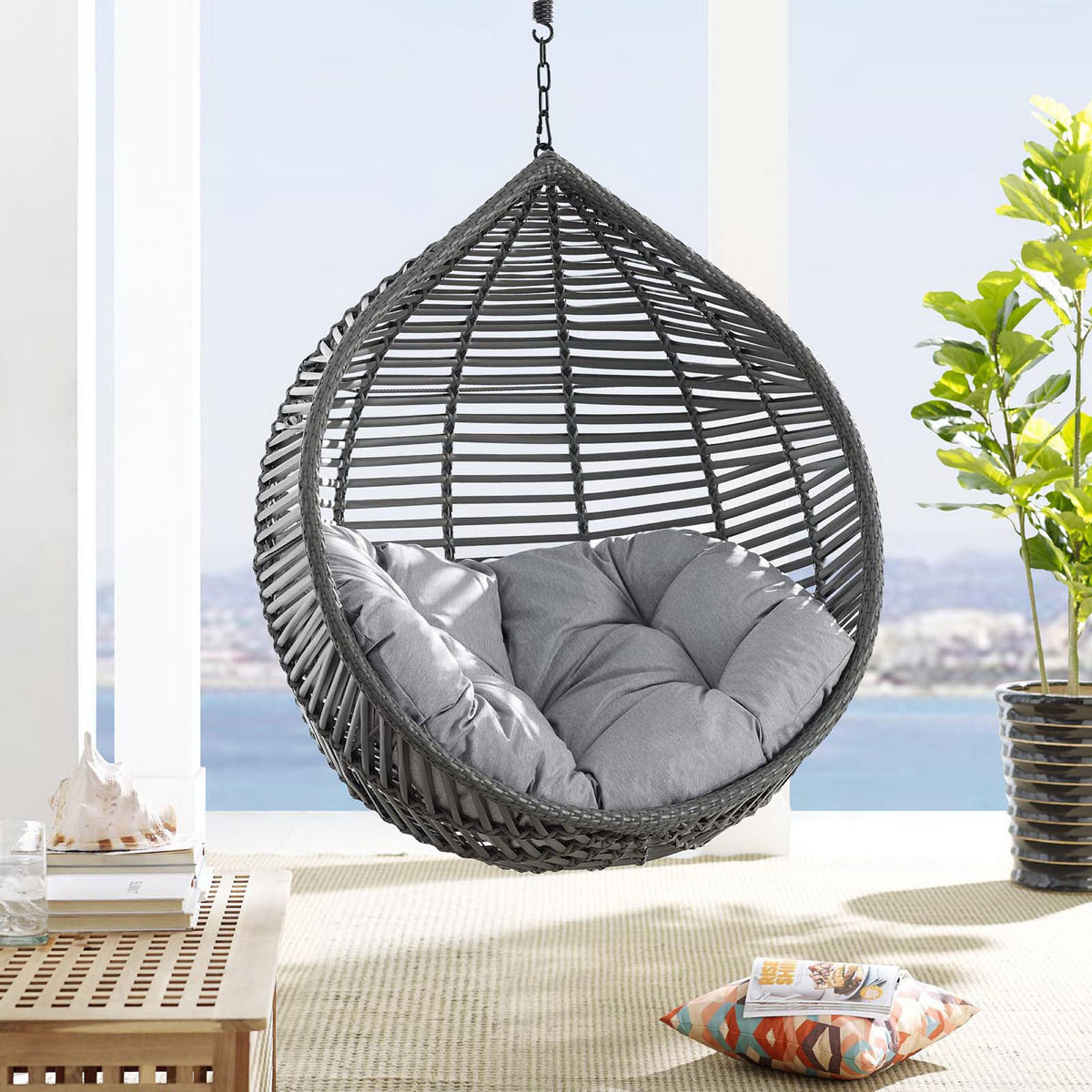 Hanging teardrop swing chair with gray cushion creating a relaxing retreat on a bright seaside balcony. || EEI-3614-GRY-GRY || front_angle_room