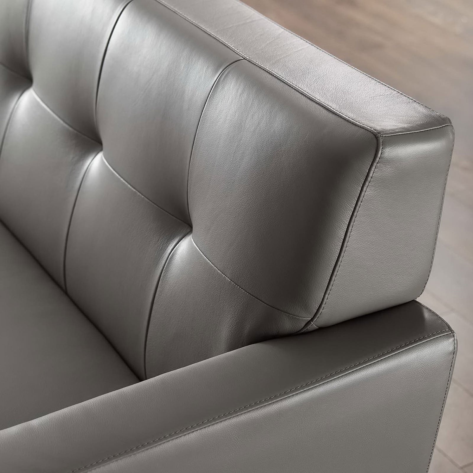 Padded gray leather armrest and tufted back cushions set above a warm wood floor in the living room || EEI-3733-GRY || detail_room