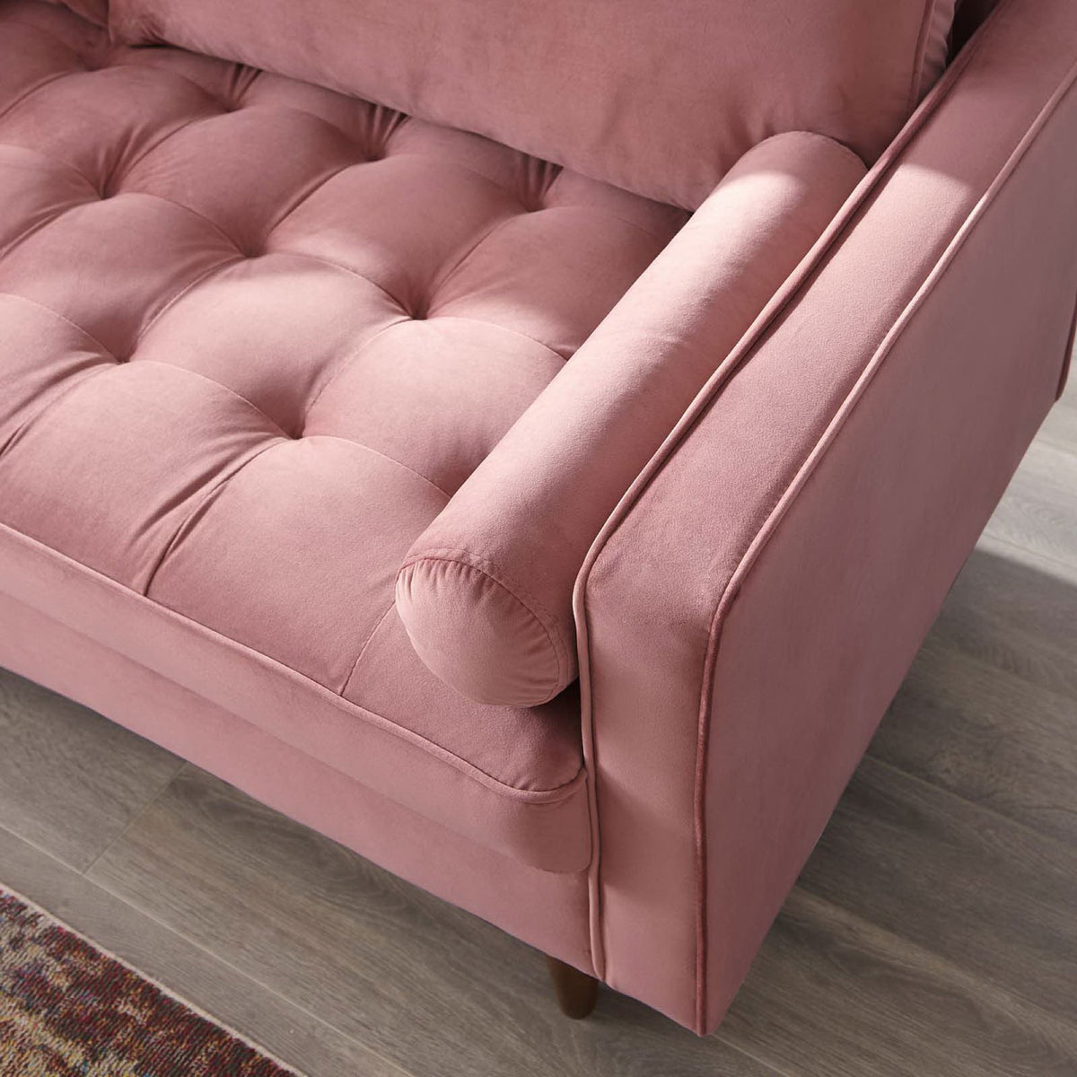 Dusty rose velvet sofa arm with bolster pillow, tufted seat, and tapered wood leg styled on a warm area rug || EEI-3764-DUS || detail_room