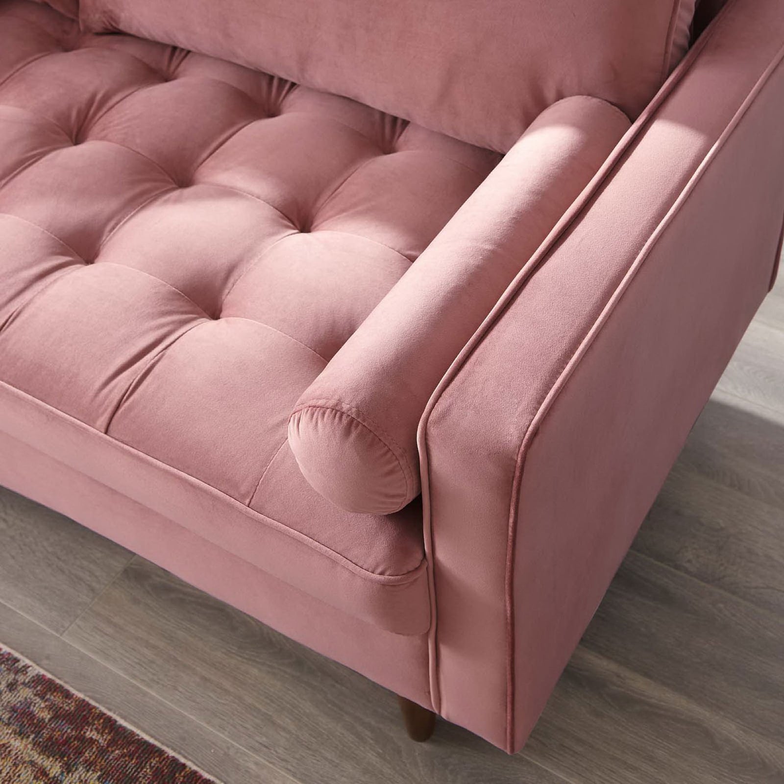 Dusty rose velvet sofa arm with bolster pillow, tufted seat, and tapered wood leg styled on a warm area rug || EEI-3764-DUS || detail_room