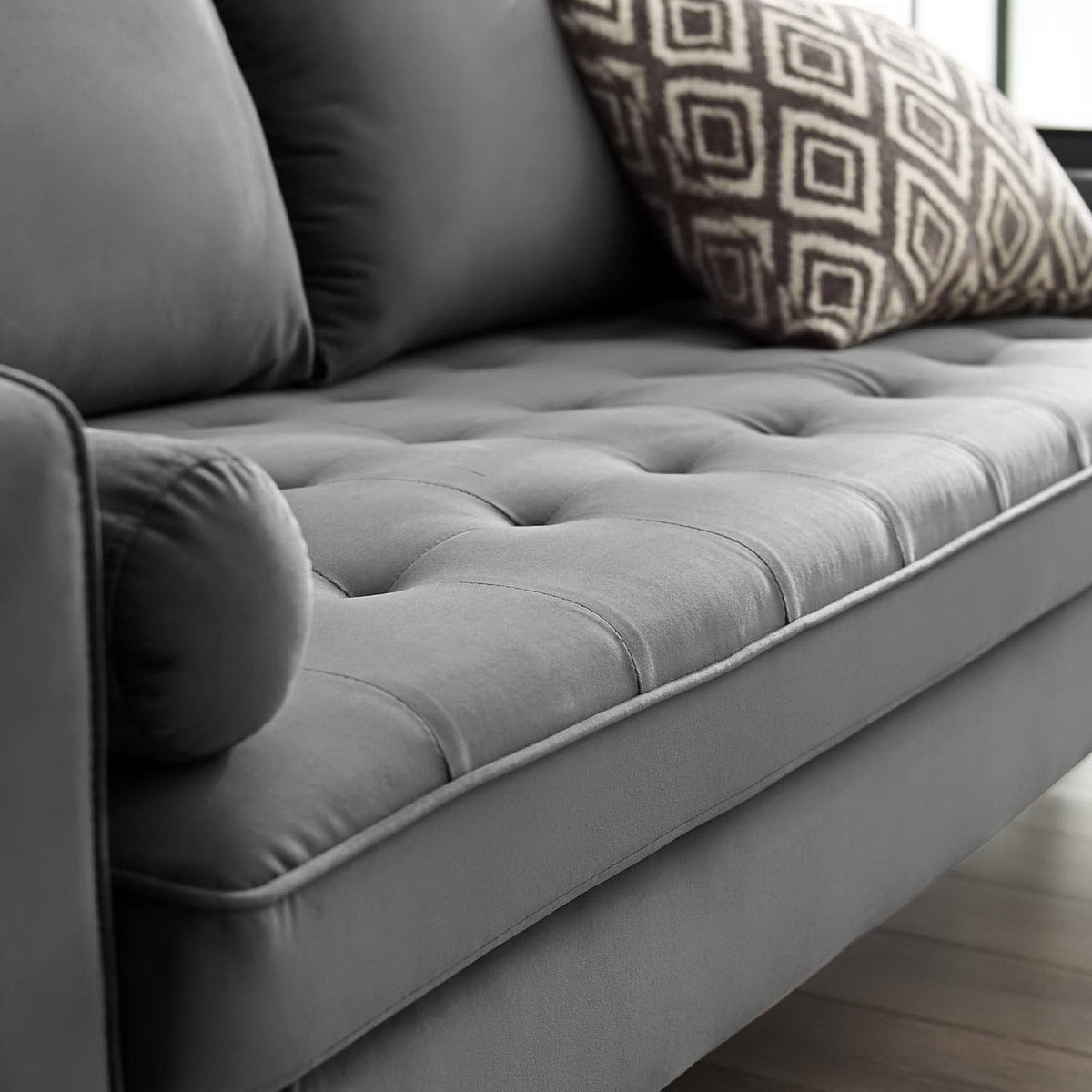 Tufted gray sofa seat with bolster pillow styled with a patterned accent cushion in a bright room || EEI-3764-GRY || detail_room