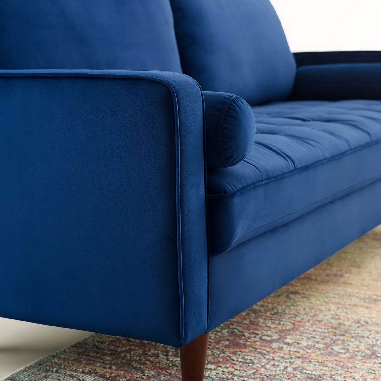 Detail of navy velvet sofa arm with bolster pillow and textured rug in a modern room || EEI-3764-NAV || detail_room