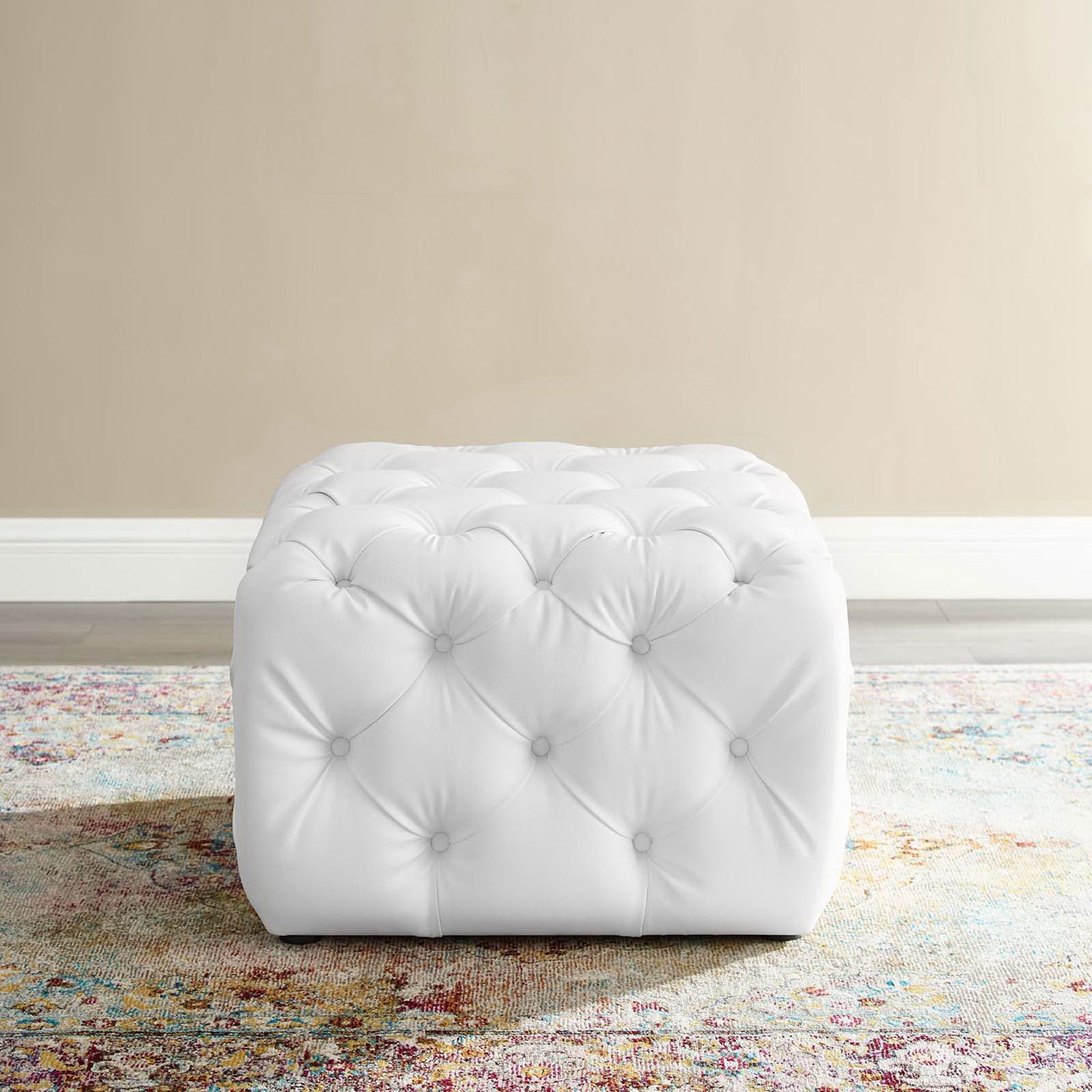 White tufted faux leather ottoman centered on a vibrant area rug in a bright living space || EEI-3775-WHI || front_room