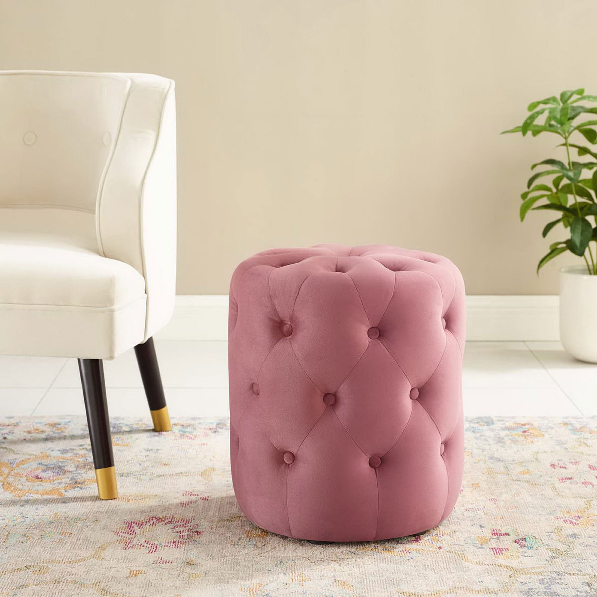 Round dusty rose velvet ottoman brings chic tufted seating to a bright living room with modern chair and greenery. || EEI-3778-DUS || front_angle_room