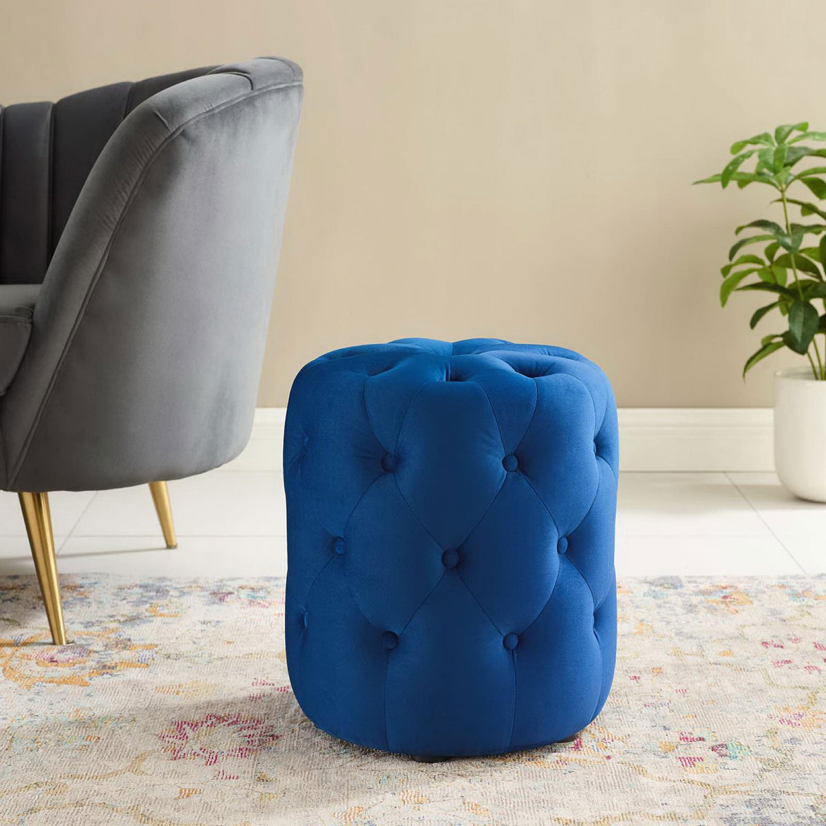 Navy velvet ottoman adding a bold pop of color beside a gray chair and greenery in a modern room || EEI-3778-NAV || front_angle_room