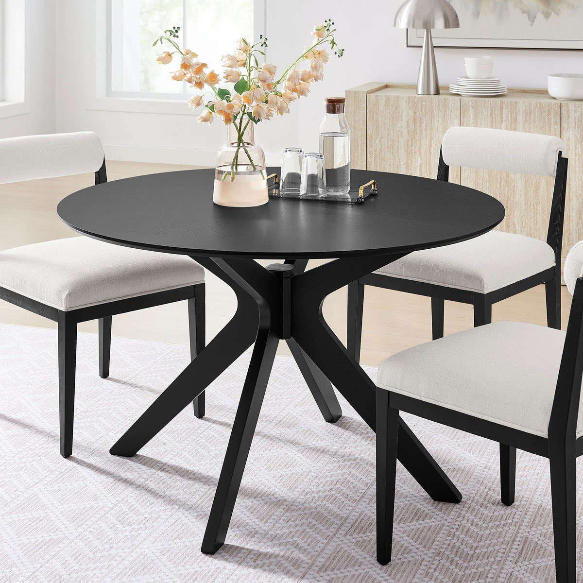 Black round dining table styled in a bright modern dining room with coordinating upholstered chairs || EEI-3847-BLK || front_angle_room