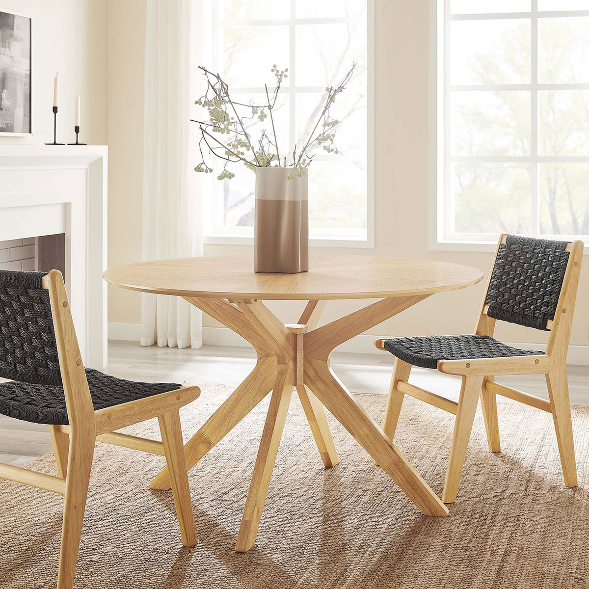 Round oak dining table with sculptural legs styled in a modern dining room with woven chairs || EEI-3847-OAK || front_angle_room