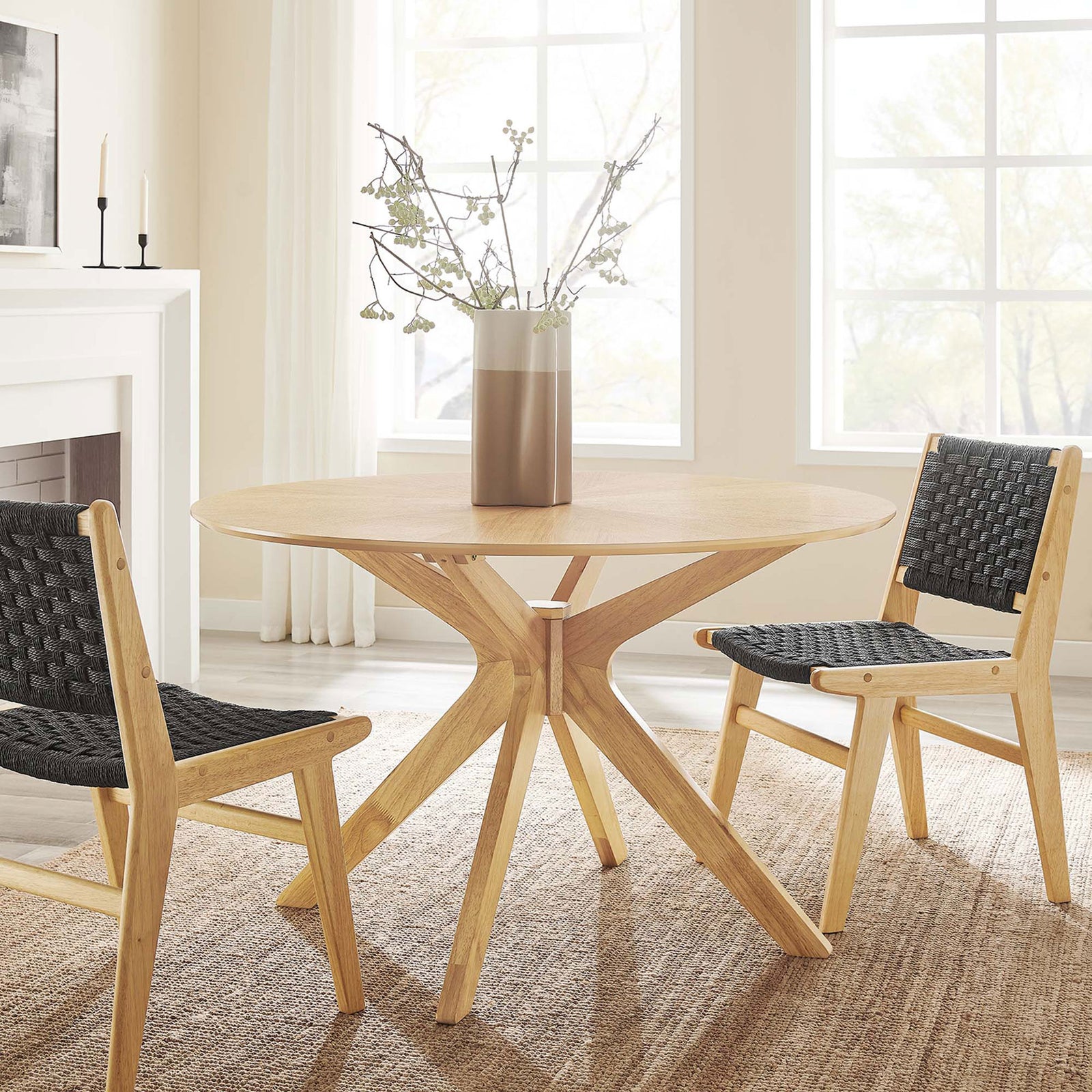 Round oak dining table with sculptural legs styled in a modern dining room with woven chairs || EEI-3847-OAK || front_angle_room