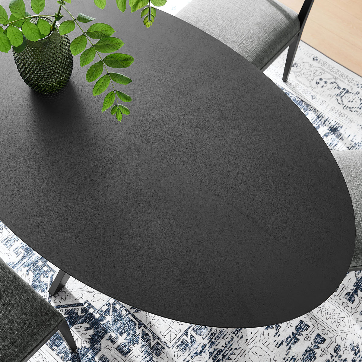 Detail of black oval tabletop styled with greenery and decor above a patterned blue and white rug || EEI-3849-BLK || detail_room